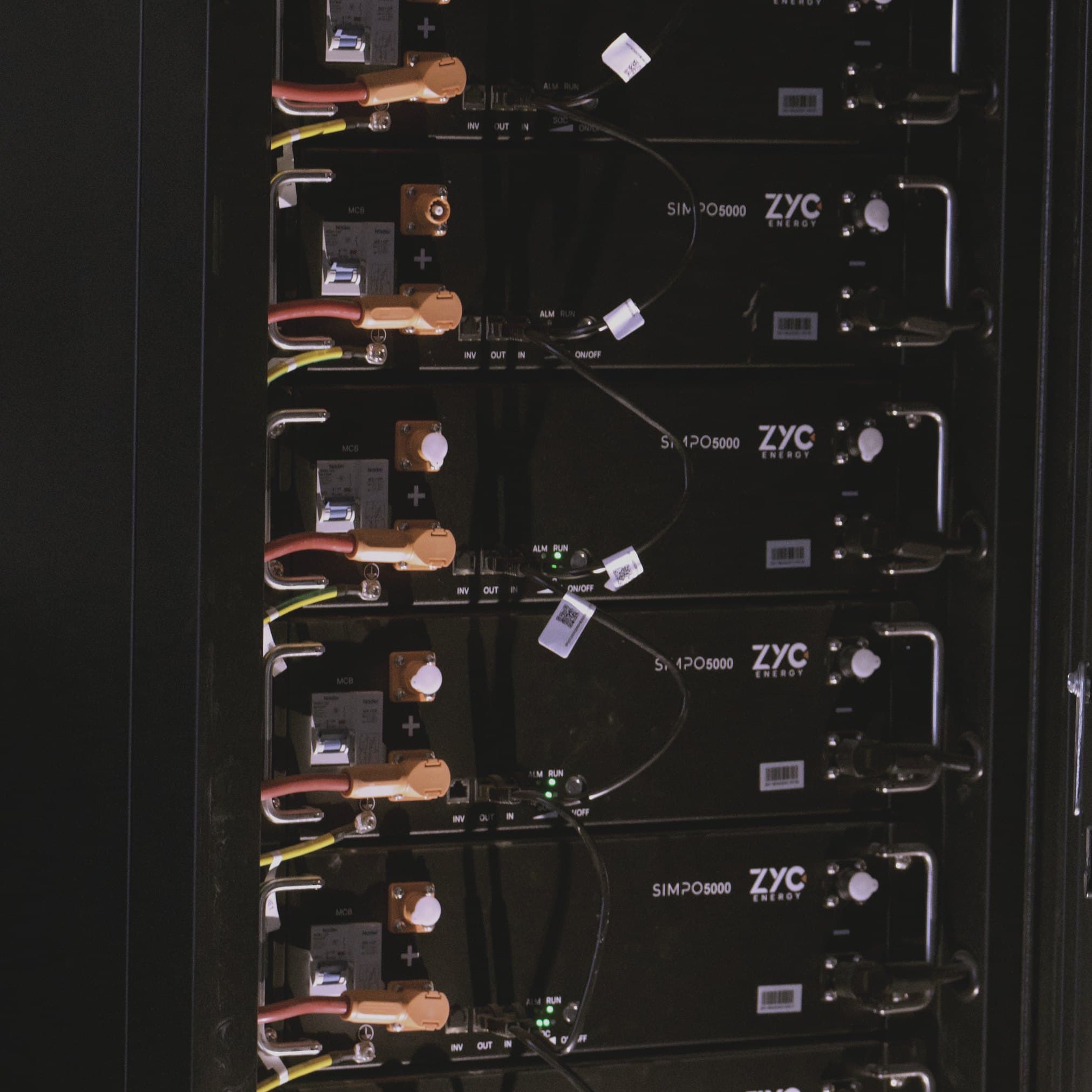 ZYC battery modules in an energy storage cabinet with orange connectors and green status LEDs.