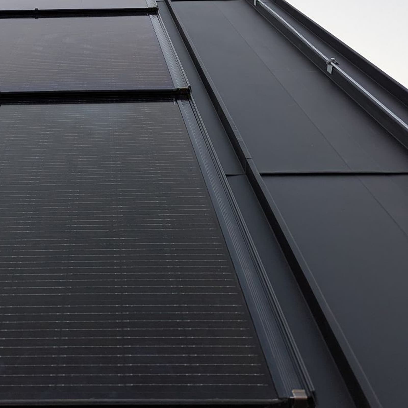 A view from below of the dark roof of a building, combining integrated photovoltaic panels with smooth, black sheet metal.