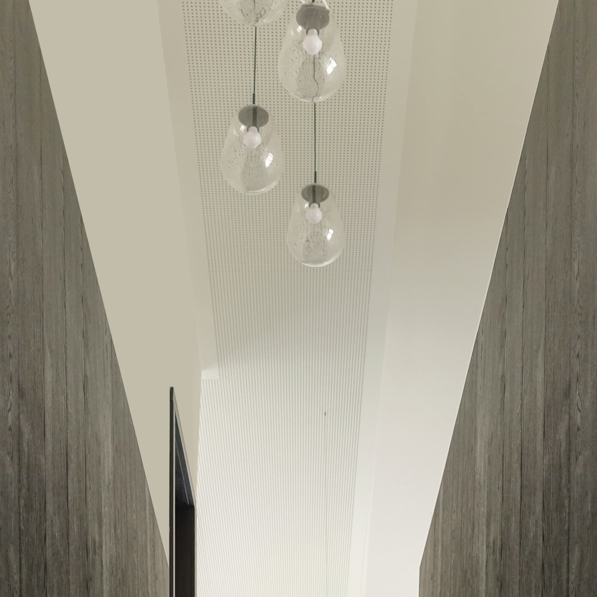 Modern, organic-shaped glass pendant lamps hanging from a white, perforated ceiling.