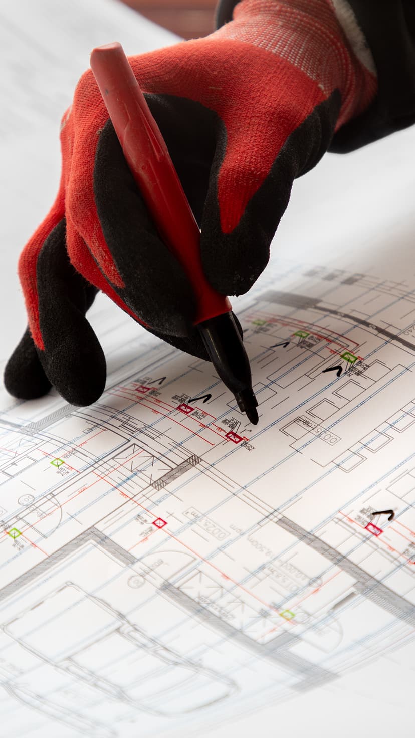 A gloved hand marking technical decisions on detailed building plans.