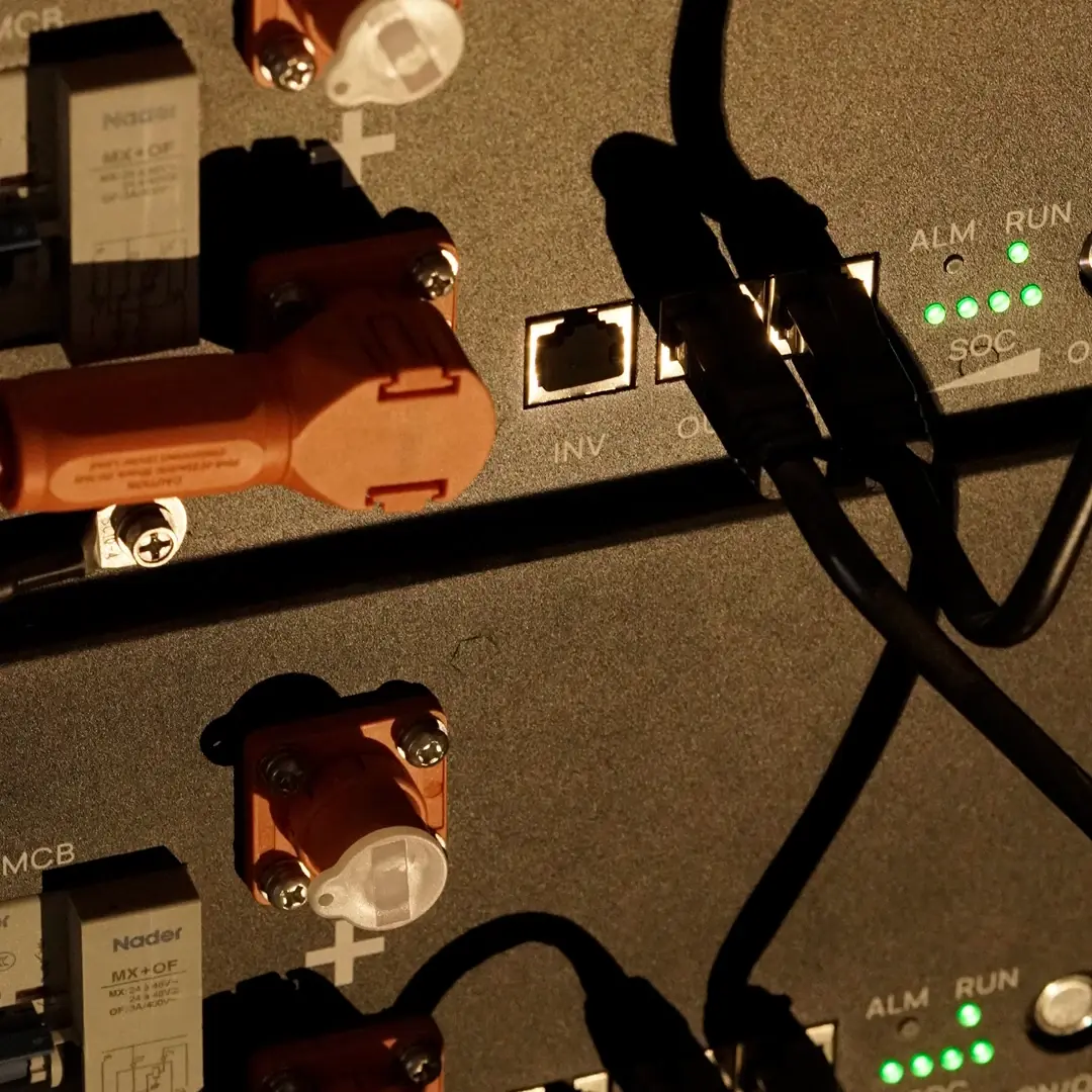 Close-up of energy storage battery modules with orange connectors, connected communication cables and green status LEDs.