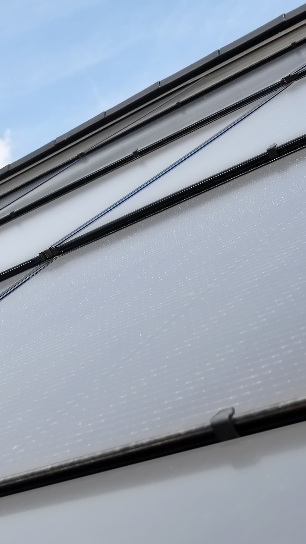 A close-up of a roof slope made of integrated photovoltaic panels in a brick-red color.
