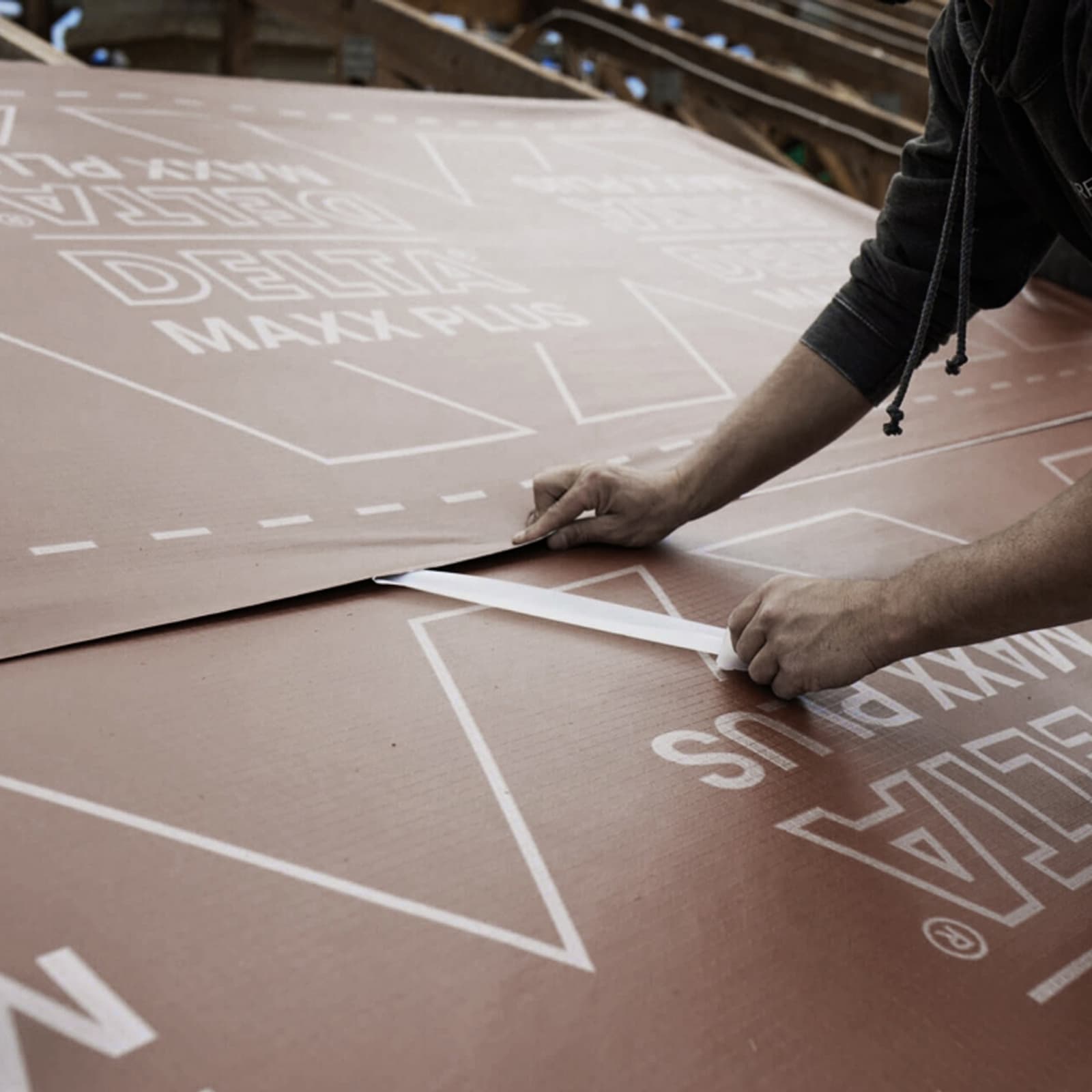 A worker is installing a large sheet of brown roof membrane with white lettering.