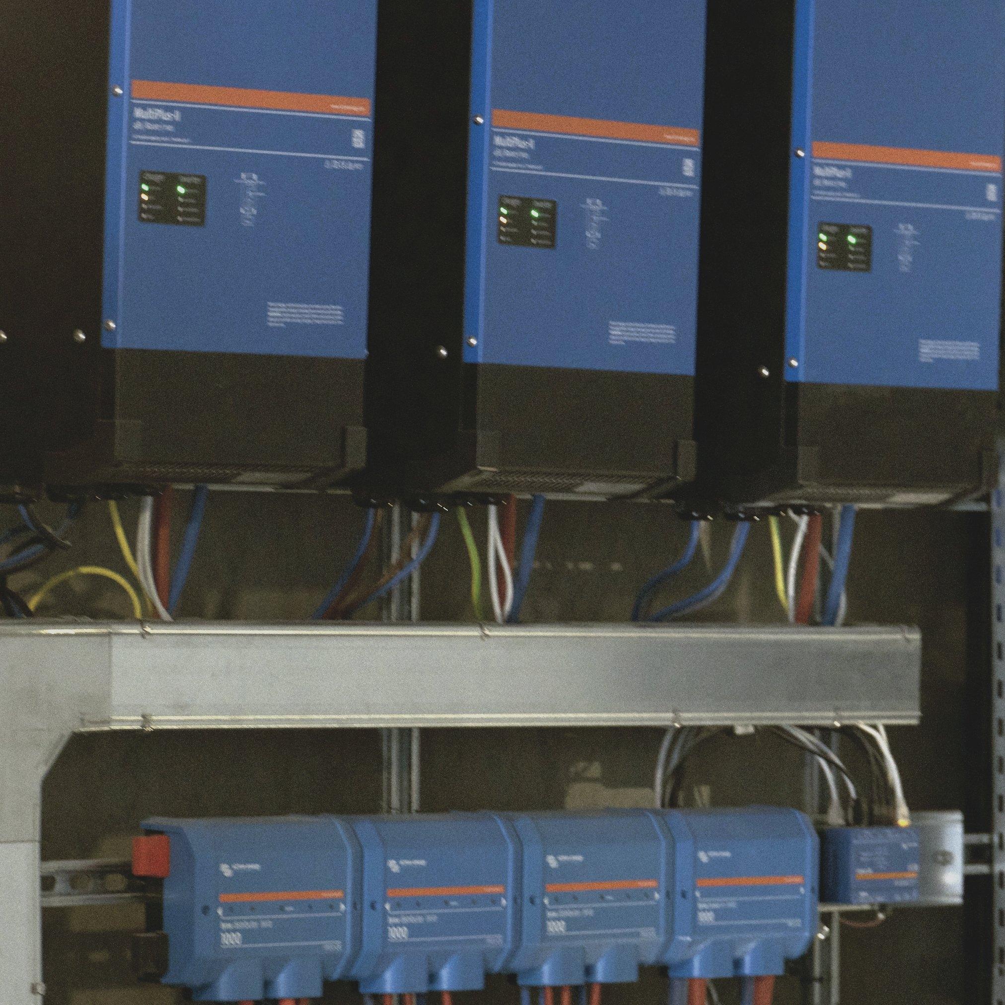 Victron MultiPlus-II inverters and charge controllers mounted next to an energy storage cabinet.