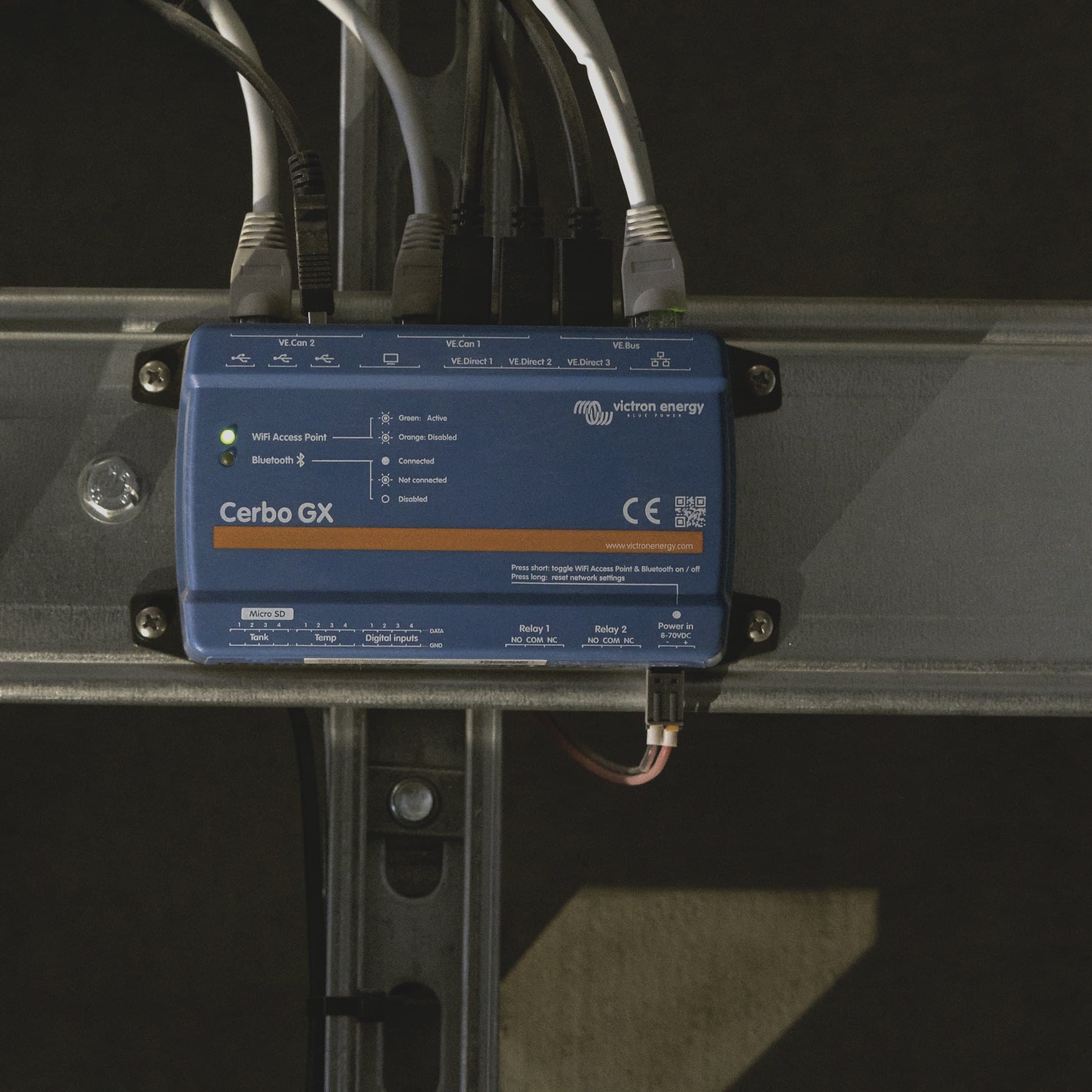 A Victron Cerbo GX controller on a DIN rail with communication cables connected.